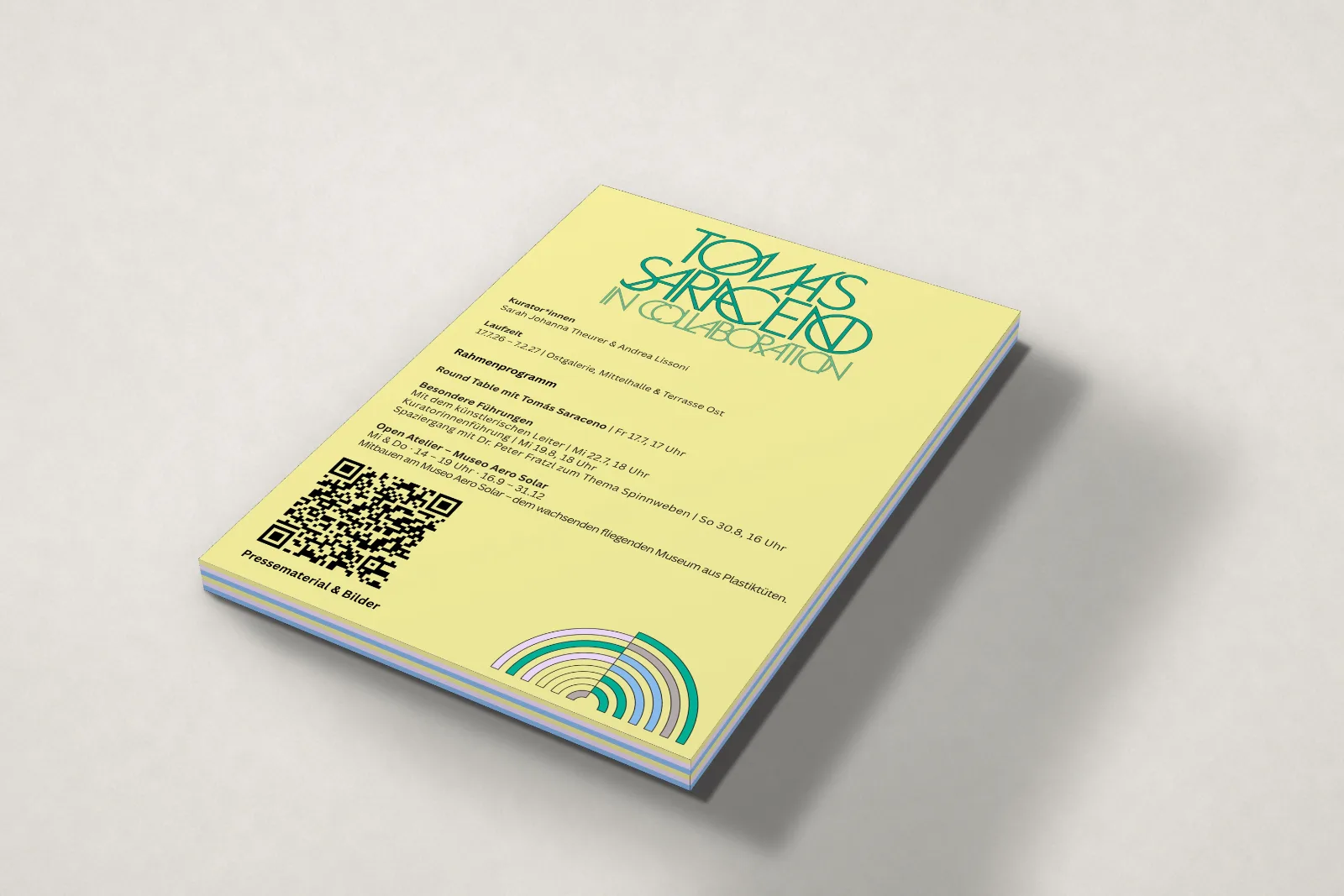 Ein Stapel Notizblöcke mit gelbem Deckblatt: Titel „Tomás Saraceno in collaboration“, Laufzeit, Rahmenprogramm, QR-Code und ein Regenbogen aus Bögen in den Hausfarben.